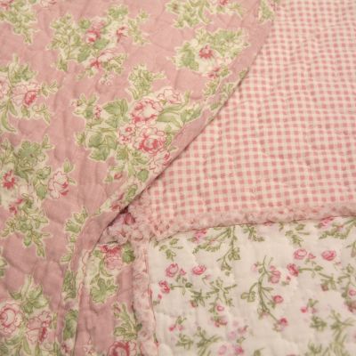 Strawberry Garden quilt set in hues of pink, white and green displayed on a bed. Comes with a quilt and two matching shams.
