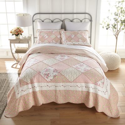 Strawberry Garden quilt set in hues of pink, white and green displayed on a bed. Comes with a quilt and two matching shams. 