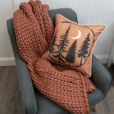 This fun decorative pillow is orange with a forest silhouette and crescent moon.